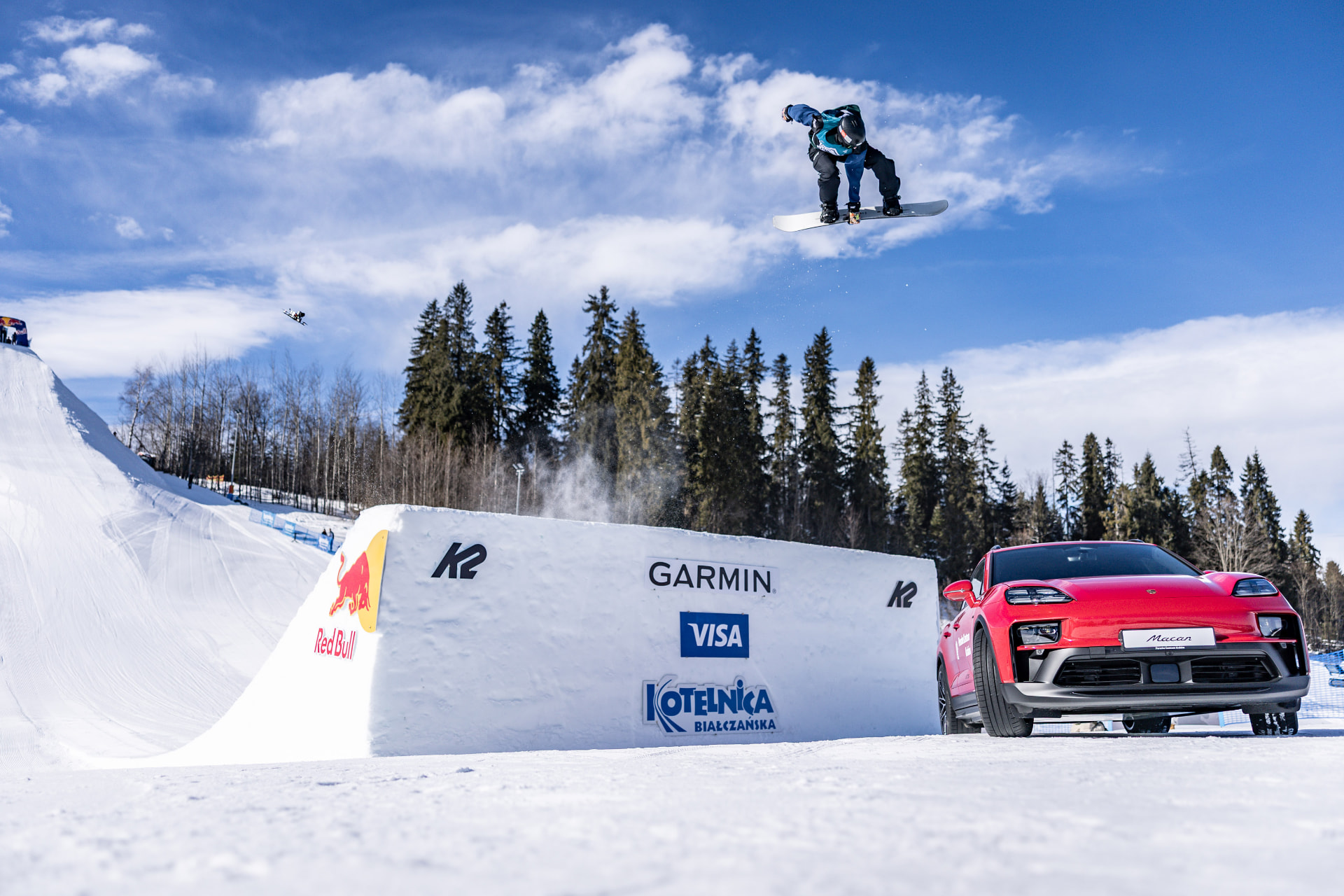 Snowboardzista z chwytem deski nad elementem śnieżnym obok samochodu
